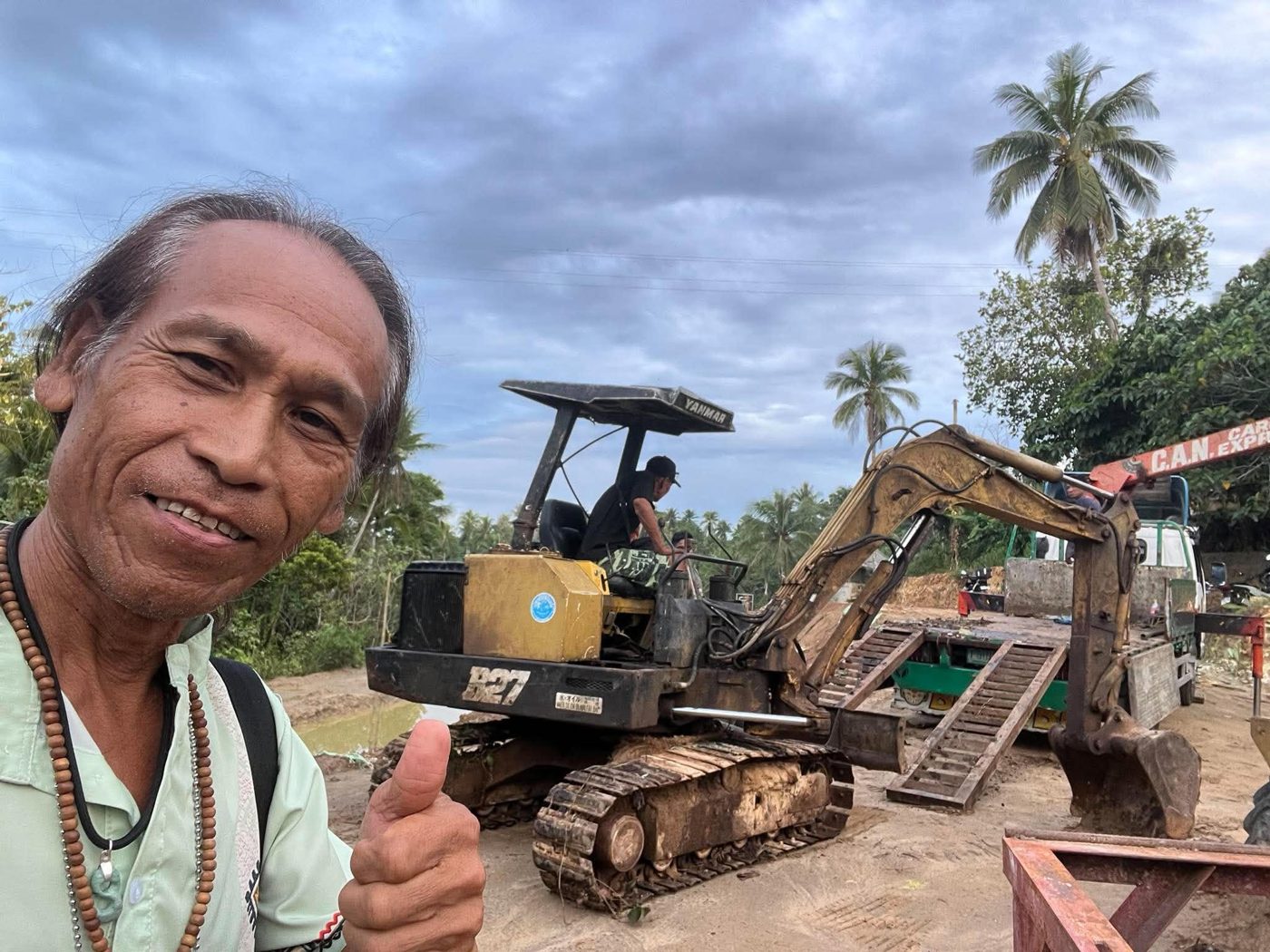 Allan Inocalla gives a thumbs-up in front of a Yanmar mini excavator being unloaded from a truck