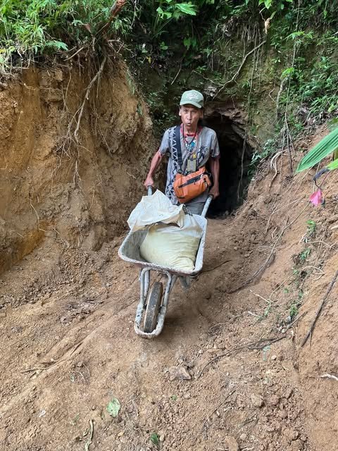 Allan Inocalla pushes a wheelbarrow with a bag of ore out of a tunnel entrance