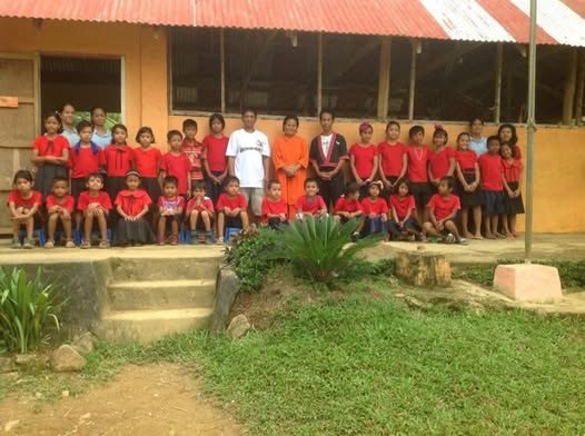 Students of AMSAI School in red uniforms with their teachers in front of the school building