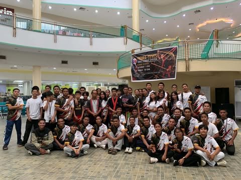 A large group of Arnis students and instructors in team shirts at a training event in a mall atrium