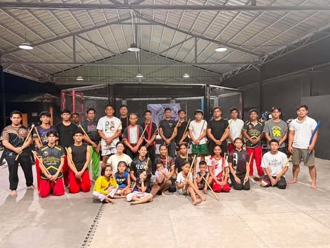 Children, young people and coaches with Arnis sticks in a martial arts gym
