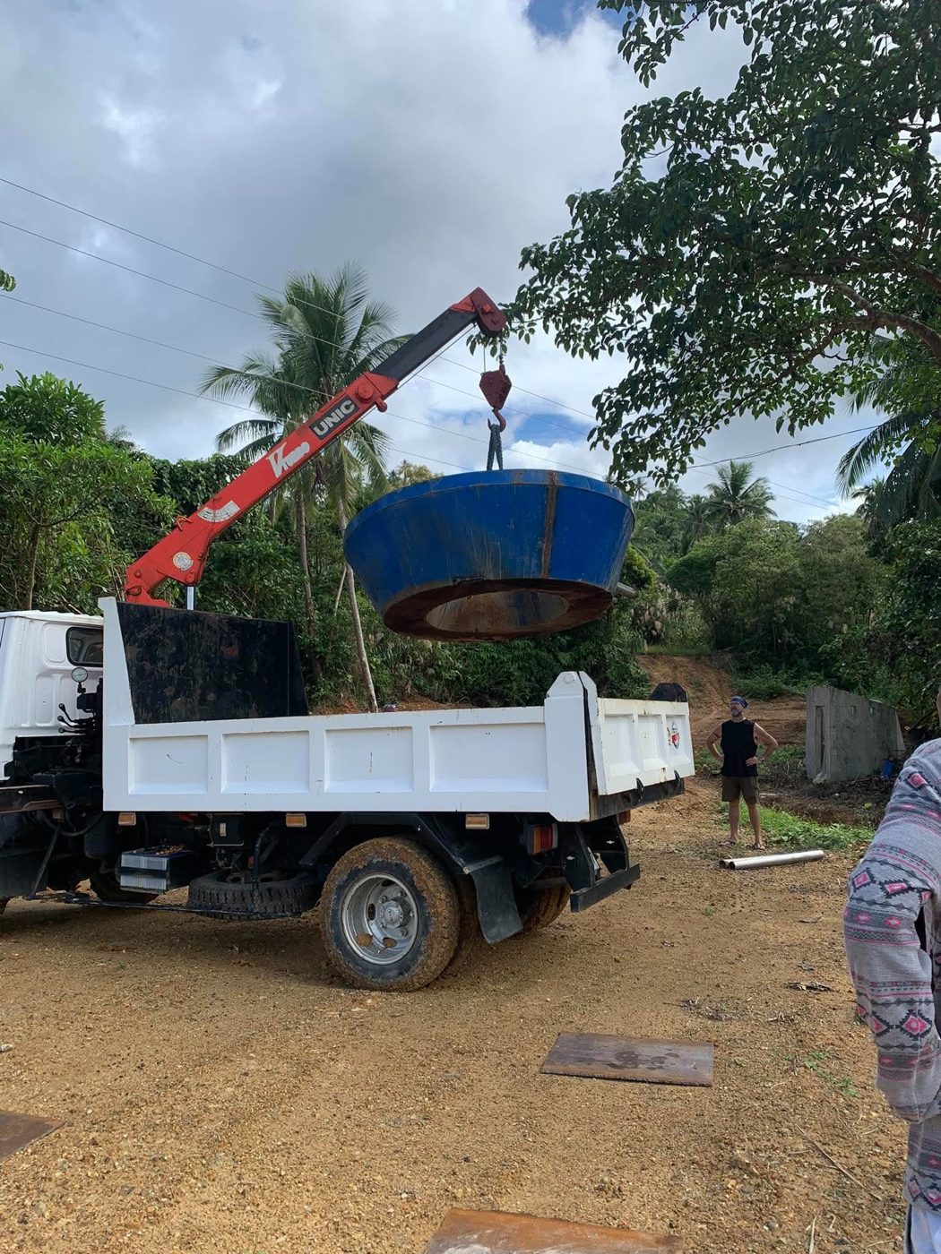 A truck-mounted crane lifts a large blue steel part for the processing plant