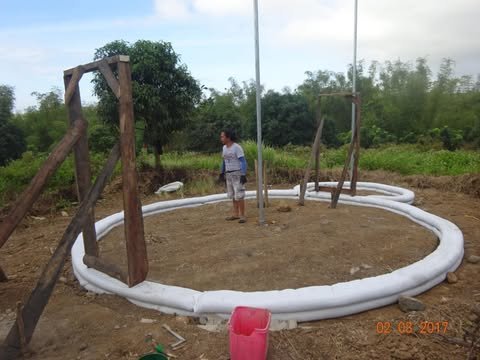 The first ring of earthbags laid in a circle on cleared ground, with a wooden frame and a centre pole