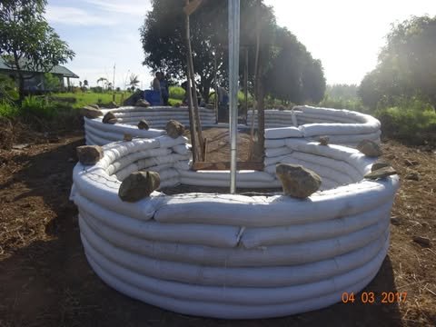 Earthbag walls rising in rings, with stones set along the top