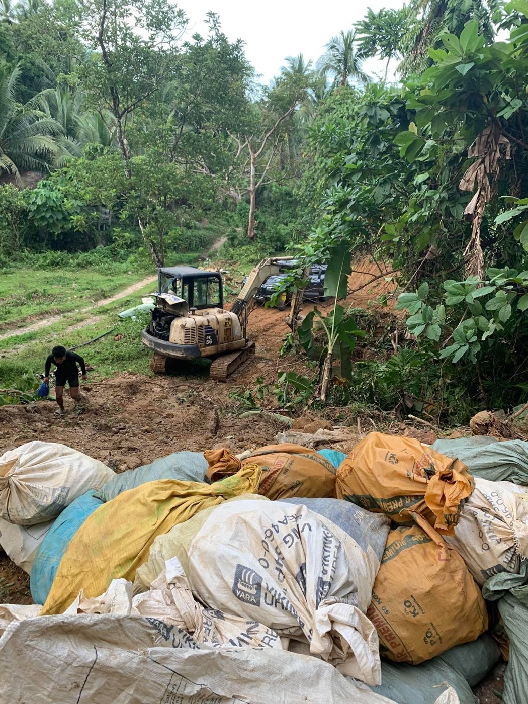 A small excavator working a hillside in the Minahang Bayan, with sacks of ore in the foreground