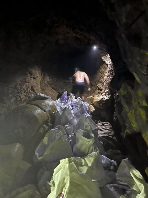 Bags of ore stacked inside a narrow tunnel while a miner with a headlamp works further in